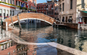 Bridge over a Venetian canal, the nearly street has flooded slightly and reflects the buildings above